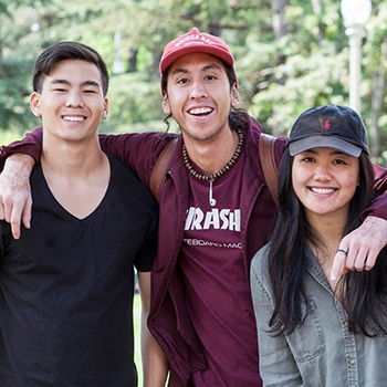 Two male and one female APASS student with arms around each others neck smiling for the camera.